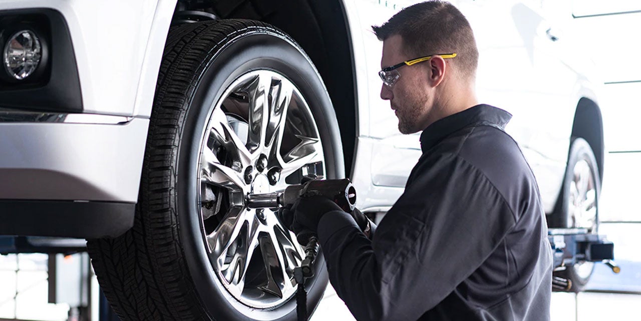A man kneels beside a car, focused on changing a tire with tools scattered around him.