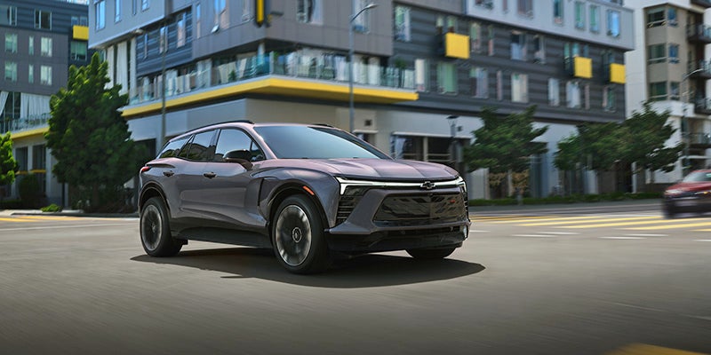 A 2025 Chevrolet Blazer EV driving along a bustling city street, showcasing its sleek design and urban environment.
