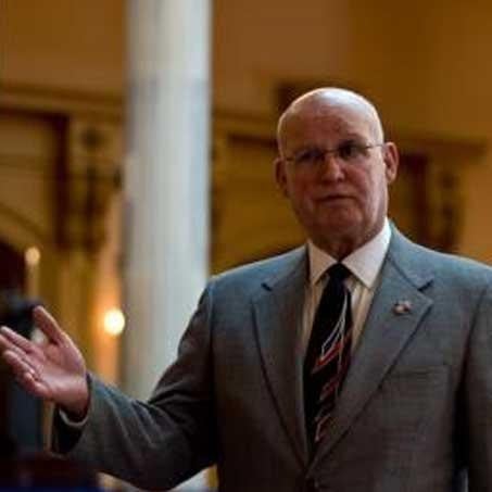 A bald man in a suit and tie stands confidently at a podium, ready to speak to an audience.