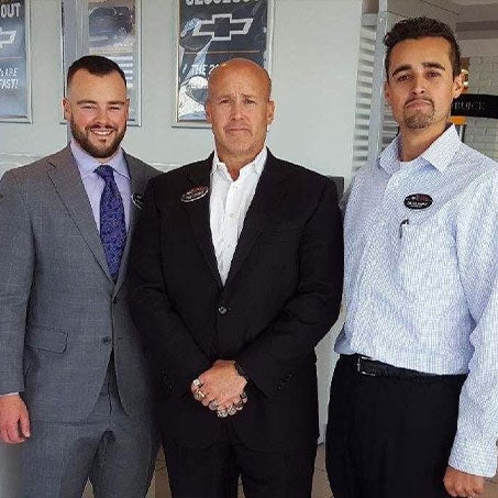 Three men in suits standing side by side, smiling and looking towards the camera.