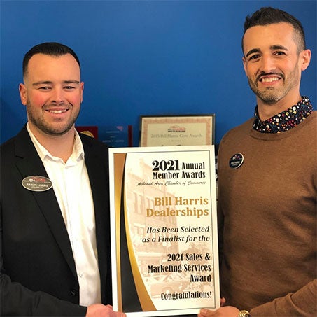 Two men proudly hold an award plaque in front of a blue wall, smiling at the camera.