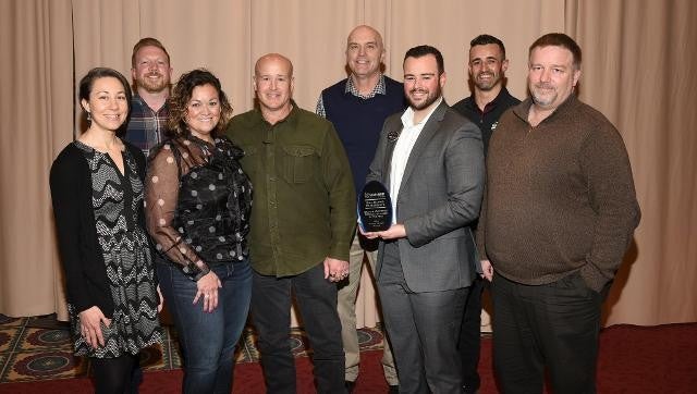 A diverse group of people standing together, proudly holding an award in celebration.