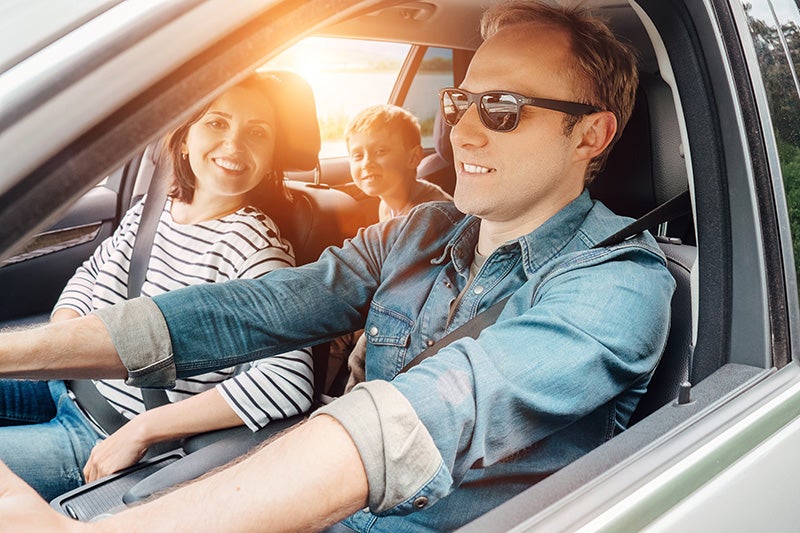 A man and woman sitting in the front seats of a car, both looking ahead with smiles on their faces.