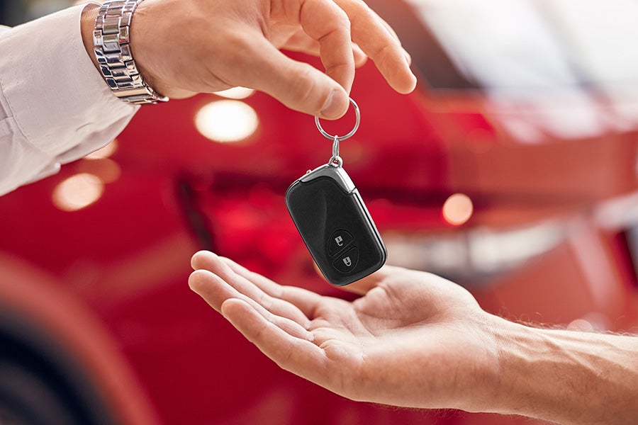 A man hands a car key to another person, symbolizing a transfer of ownership or responsibility.